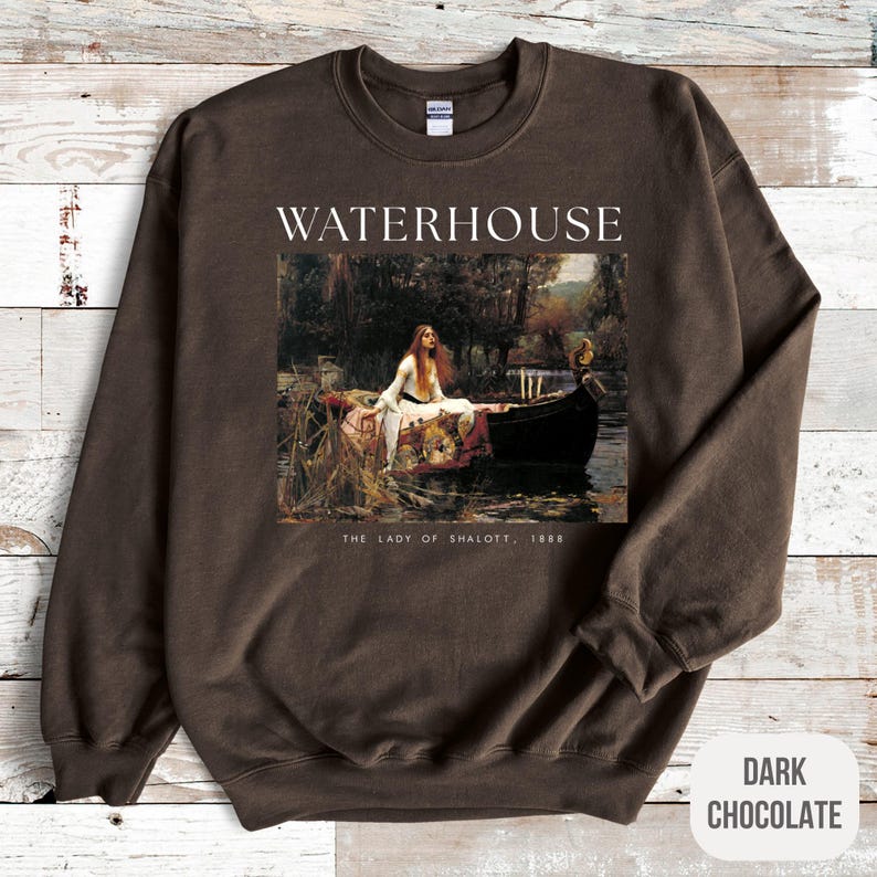 May include: A brown sweatshirt with the text "WATERHOUSE" printed in white on the front. The sweatshirt features a painting of a woman in a boat with the text "THE LADY OF SHALOTT, 1888" printed below the image. The sweatshirt is labeled "DARK CHOCOLATE".