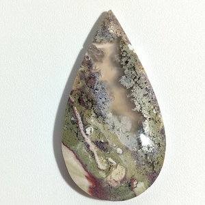 May include: A teardrop-shaped cabochon of agate with a green, white, and brown pattern. The stone has a polished surface and is translucent.