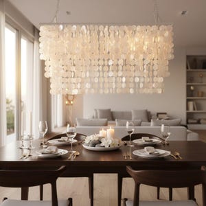 May include: A rectangular chandelier featuring multiple tiers of translucent, circular capiz shell discs suspended from a metal frame. The light fixture hangs above a dining table set with white plates, glassware, and a centerpiece of candles.