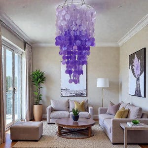 Puede incluir: Un salón moderno con una gran y llamativa lámpara de araña. La lámpara de araña está compuesta por numerosos elementos en forma de disco de color púrpura y lavanda. La habitación también incluye dos sofás, una mesa de centro redonda y una planta en maceta.