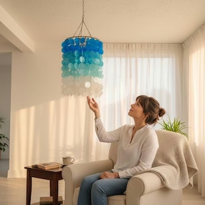 Puede incluir: Una lámpara colgante con forma cilíndrica, compuesta por numerosos discos redondos y translúcidos. Los discos cambian de color de azul oscuro en la parte superior, pasando por azules más claros, hasta blanco en la parte inferior. La lámpara cuelga de una cadena.