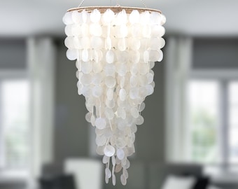 May include: A white shell chandelier with a circular base and multiple layers of shells hanging down. The shells are arranged in a cascading pattern, creating a unique and elegant look.