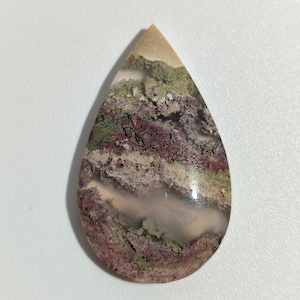 Può includere: Un cabochon di agata a forma di lacrima con un motivo a strati di rosa, bianco, verde e marrone. La pietra ha una finitura lucida.