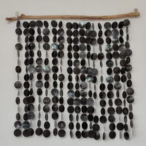 Op de afbeelding: Een zwart en zilveren kralen gordijn gemaakt van ronde, overlappende schijven hangt aan een houten stok. Het gordijn is ongeveer 76 cm breed en 102 cm lang.
