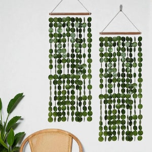 May include: Two green beaded wall hangings. Each has a wooden rod at the top with strings of green, circular beads hanging down. The beads are various shades of green. The hangings are suspended from the wall by a string.