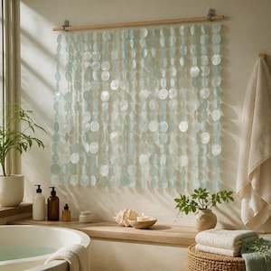May include: A wall hanging composed of multiple vertical strands of circular, translucent, pale blue shell discs suspended from a horizontal wooden rod. The discs have a pearlescent finish and are arranged in a grid-like pattern across the wall.