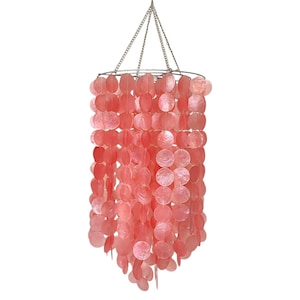 Op de afbeelding: Een roze schelp kroonluchter met een zilveren ketting die aan het plafond hangt. De kroonluchter is gemaakt van veel kleine, ronde schelpen die in een cascadepatroon aan elkaar geregen zijn.