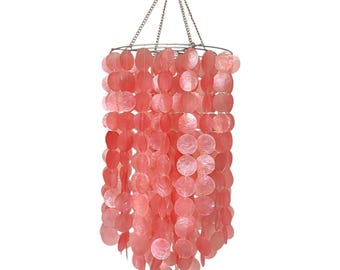 May include: A pink shell chandelier with a silver chain hanging from the ceiling. The chandelier is made of many small, round shells that are strung together in a cascading pattern.
