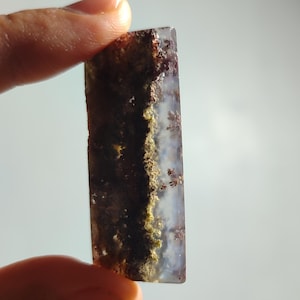 Puede incluir: Una pieza rectangular de ágata con un patrón de color blanco, gris y marrón. La ágata tiene una textura rugosa y natural.