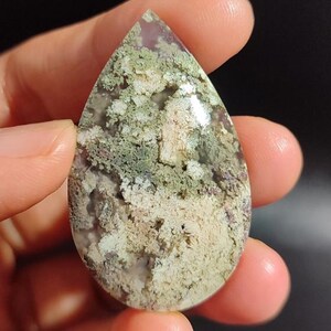 May include: A teardrop-shaped green and white agate cabochon with a dendritic pattern. The agate is translucent and has a smooth, polished surface.