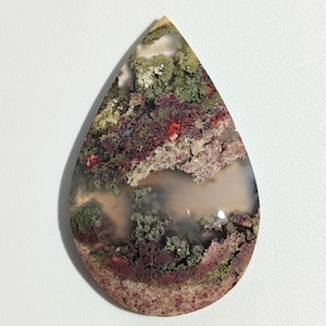 May include: A teardrop-shaped agate cabochon with a unique pattern of red, green, and white dendrites. The stone has a translucent appearance and a smooth, polished surface.