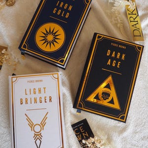 May include: Three hardcover books with gold foil lettering and illustrations. The titles are "Iron Gold", "Dark Age", and "Light Bringer". All three books are by Pierce Brown.