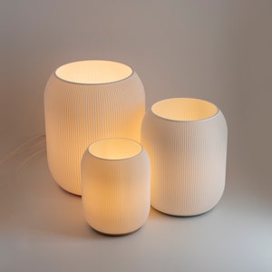 Könnte beinhalten: Drei weiße Keramiklampen mit gerippten Designs, die größte Lampe ist hinten und die kleinste Lampe vorne.