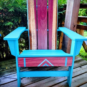 May include: A handcrafted Adirondack chair with a vibrant design. The chair features a turquoise frame and armrests, complemented by a backrest of mixed wood tones, including deep red and natural wood. The seat has a red panel with turquoise geometric accents.