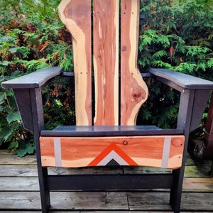May include: A handcrafted Adirondack chair with a natural wood back and seat, featuring a unique live edge design. The chair has black armrests and legs, and the front panel is decorated with an orange and gray geometric pattern.