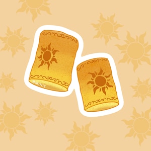Puede incluir: Dos linternas de papel amarillas con un diseño de sol y un borde blanco. Las linternas están sobre un fondo naranja claro.