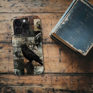 May include: A black phone case with a collage design featuring a raven, moons, and vintage-looking paper scraps. The case has a camera lens cutout.