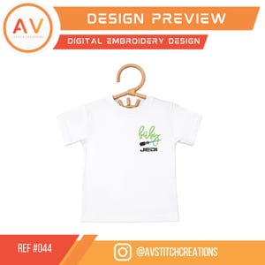 K&ouml;nnte beinhalten: Wei&szlig;es Baby-T-Shirt mit einem gr&uuml;n-blauen "Baby Jedi"-Design. Das Design enth&auml;lt eine Lichtschwert-Grafik. Das Shirt h&auml;ngt an einem Holzkleiderb&uuml;gel. Oben im Bild steht "DESIGN PREVIEW" und "DIGITAL EMBROIDERY DESIGN".