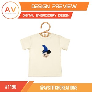 Op de afbeelding: Cr&egrave;mekleurig T-shirt met een Mickey Mouse-ontwerp met een blauwe tovenaarsmuts. Het shirt wordt op een houten hanger getoond. De bovenkant van de afbeelding luidt "DESIGN PREVIEW" en "DIGITAL EMBROIDERY DESIGN". De onderkant van de afbeelding luidt "#1190" en "@AVSTITCHCREATIONS".