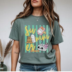 Cute Summerween ghost shirt design with striped background, ghost building sandcastle, ghost on float, skull coconut drink and tropical spooky summer aesthetic