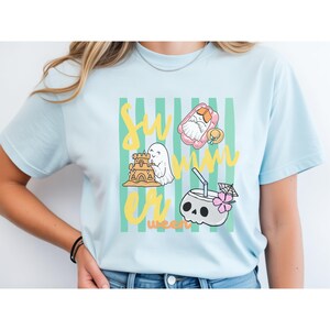 Cute Summerween ghost shirt design with striped background, ghost building sandcastle, ghost on float, skull coconut drink and tropical spooky summer aesthetic