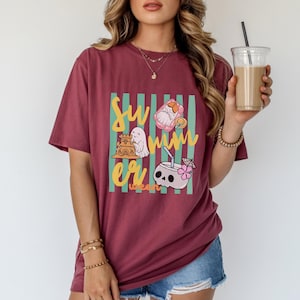Cute Summerween ghost shirt design with striped background, ghost building sandcastle, ghost on float, skull coconut drink and tropical spooky summer aesthetic