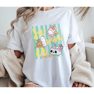 Cute Summerween ghost shirt design with striped background, ghost building sandcastle, ghost on float, skull coconut drink and tropical spooky summer aesthetic
