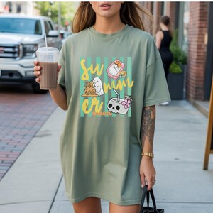 Cute Summerween ghost shirt design with striped background, ghost building sandcastle, ghost on float, skull coconut drink and tropical spooky summer aesthetic