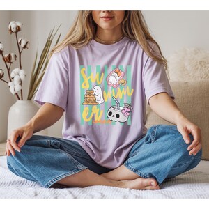 Cute Summerween ghost shirt design with striped background, ghost building sandcastle, ghost on float, skull coconut drink and tropical spooky summer aesthetic