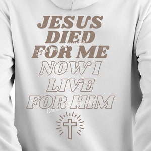 Puede incluir: Sudadera con capucha blanca con un estampado gráfico marrón que dice "Jesús murió por mí Ahora vivo para él" con una cruz y un diseño de sol radiante debajo del texto.