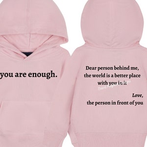 May include: Pink hooded sweatshirt with the text "you are enough." on the front and "Dear person behind me, the world is a better place with you in it. Love, the person in front of you." on the back.