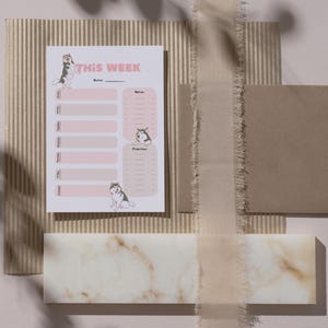 Op de afbeelding: Een roze en witte printbare weekplanner met de tekst "THIS WEEK" bovenaan. De planner heeft twee kolommen, &eacute;&eacute;n voor "Voor" en &eacute;&eacute;n voor "Na". Elke kolom bevat een lijst met de dagen van de week met ruimte om taken in te vullen. De planner is versierd met illustraties van honden.