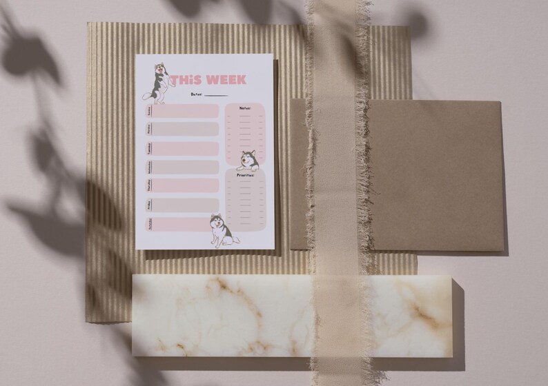 Op de afbeelding: Een roze en witte printbare weekplanner met de tekst "THIS WEEK" bovenaan. De planner heeft twee kolommen, &eacute;&eacute;n voor "Voor" en &eacute;&eacute;n voor "Na". Elke kolom bevat een lijst met de dagen van de week met ruimte om taken in te vullen. De planner is versierd met illustraties van honden.