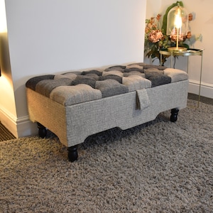 Könnte beinhalten: Eine graue und schwarze Patchwork-Aufbewahrungskiste mit einer gesteppten Oberseite und Holzbeinen. Die Kiste steht auf einem grauen Shaggy-Teppich.