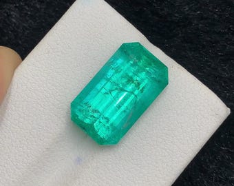 Puede incluir: Una piedra preciosa rectangular de corte esmeralda con un color verde vibrante y translúcido con inclusiones internas visibles. La piedra presenta bordes facetados que captan la luz, mostrando un tono brillante y saturado.