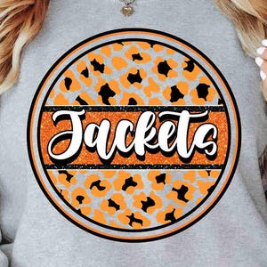 May include: A gray sweatshirt featuring a circular design with the word "Jackets" in white script. The design includes an orange and black leopard print pattern, outlined in black and orange.
