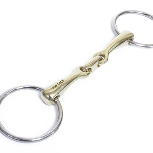 May include: A gold-coloured horse bit with a jointed mouthpiece and two stainless steel rings. The bit is engraved with the words "Top Tack".
