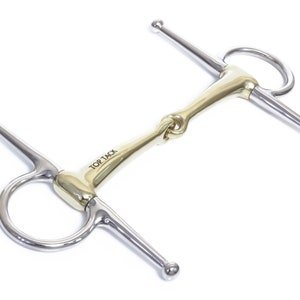 Puede incluir: Un bocado de caballo de color dorado con una boquilla y piezas de mejilla de acero inoxidable. El bocado tiene un anillo suelto a cada lado y una boquilla articulada simple. El bocado está grabado con las palabras "Top Tack".