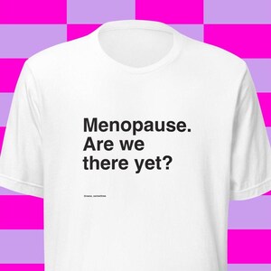 May include: White t-shirt with the text "Menopause. Are we there yet?" in black, with the @meno_sentilove social media handle below the text. The shirt is displayed against a pink and purple checkered background.