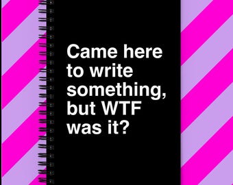 Puede incluir: Cuaderno negro con espiral con el texto blanco "Came here to write something, but WTF was it?". El cuaderno está sobre un fondo de rayas diagonales rosas y lavanda.