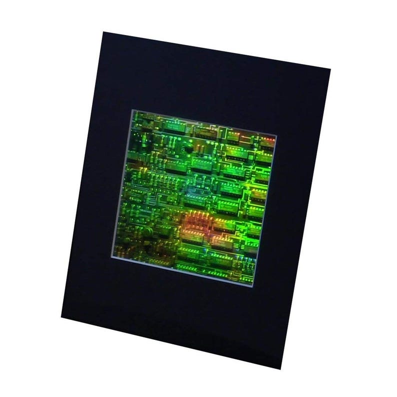Puede incluir: Una imagen enmarcada de una placa de circuito verde con fondo negro. La placa de circuito est&aacute; iluminada con un brillo verde y naranja.