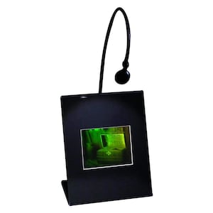 Puede incluir: Un marco de fotos negro con una luz LED incorporada. El marco está inclinado y tiene una imagen verde en su interior.