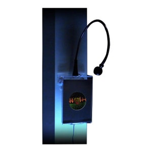 May include: A black box with a clear front panel displaying a red and orange graphic of a heart beat and a circle with a grid pattern. A black flexible gooseneck lamp is attached to the top of the box.