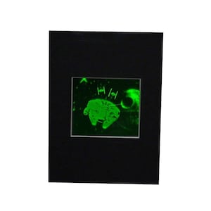 May include: A black framed image of a green spaceship with a black background. The spaceship is flying through space with a planet in the background.