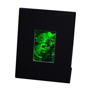 May include: A black display case featuring a glowing green image of a creature with sharp teeth and a detailed, textured design. The image is rectangular and centered within the case, which has a simple, clean design.