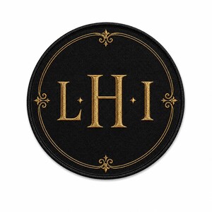 May include: A circular black embroidered patch featuring the gold-stitched letters L, H, and I in the center. The design includes a thin gold circular border with decorative fleur-de-lis accents at the top, bottom, and sides of the emblem.