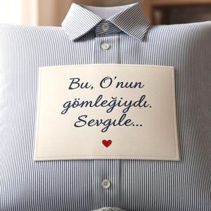 May include: A blue and white striped pillow with a shirt collar and button detail. A rectangular patch with the text "Bu, O'nun gömleğiydi. Sevgili..." and a small red heart is sewn onto the pillow.