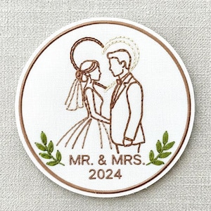 May include: Embroidered wedding patch featuring a bride and groom silhouette within a heart-shaped design. The patch includes the text "MR. & MRS. 2024" and decorative green leaves. The design is on a white background with a brown border.