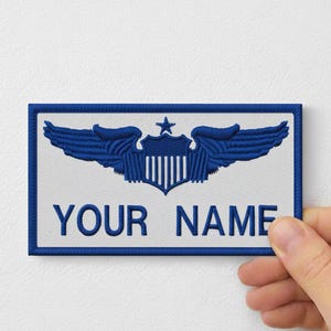 May include: Embroidered patch with a blue and white design. The patch features a shield with wings and a star, with the text "YOUR NAME" in blue. The patch is rectangular with a blue border.