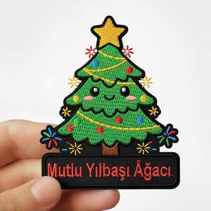Peut inclure: Écusson brodé représentant un sapin de Noël vert avec des ornements colorés, une étoile jaune et le texte "Mutlu Yılbaşı Ağacı" sur une bannière noire. Le patch a un design mignon et cartoon.